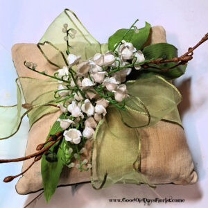 Decorative bouquet of white flowers and green leaves tied with a gold ribbon on a beige wrapped gift