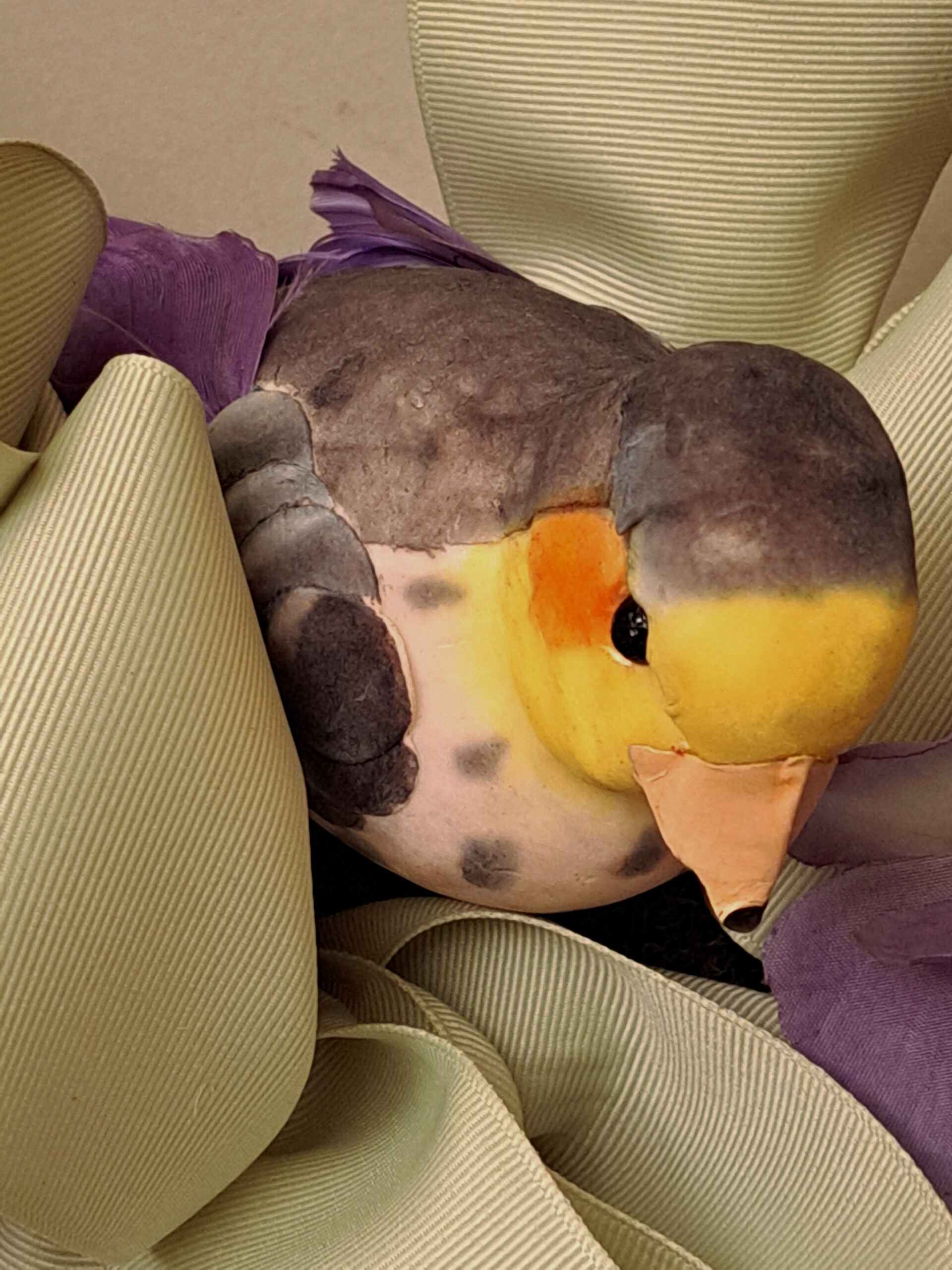 Close-up of a yellow and brown plush duck tucked among green corduroy cushions with a purple feathered tail showing mainly.